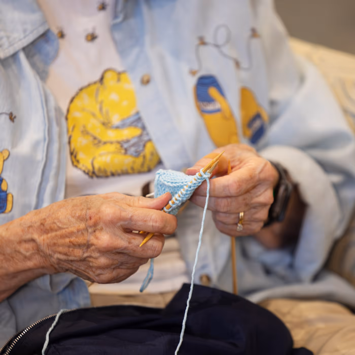 An elderly person is knitting with light blue yarn, focusing on their hands and needles.