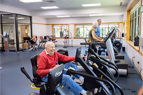 Older adults exercising on stationary bikes and treadmills in a fitness center.