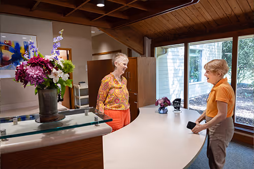 Two women talking at a reception desk in a bright, modern office space.