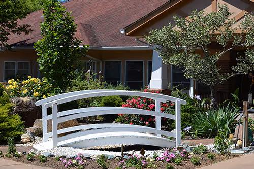 A small white wooden bridge surrounded by colorful flowers in front of a house.
