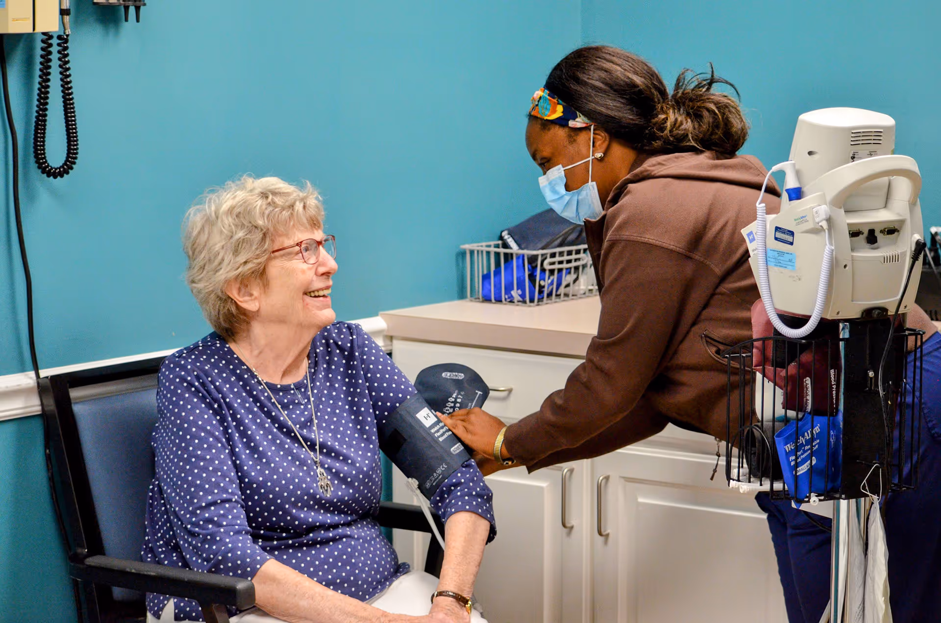 A nurse checks an older woman's blood pressure in a medical office.