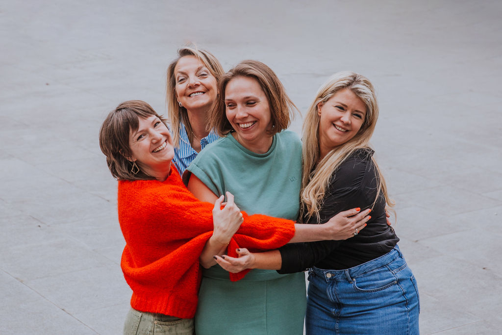 Four professional women embracing and laughing together in an outdoor setting, reflecting strong team unity, positive workplace relationships, and inclusive company culture. This image is ideal for business websites, leadership branding, and team-focused marketing materials.