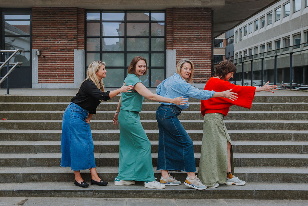 Four professional women lined up in a playful pose on outdoor steps, symbolizing teamwork, creativity, and workplace fun. Their coordinated yet casual outfits and lighthearted demeanor promote a strong sense of company culture, collaboration, and women-led leadership in modern business environments.