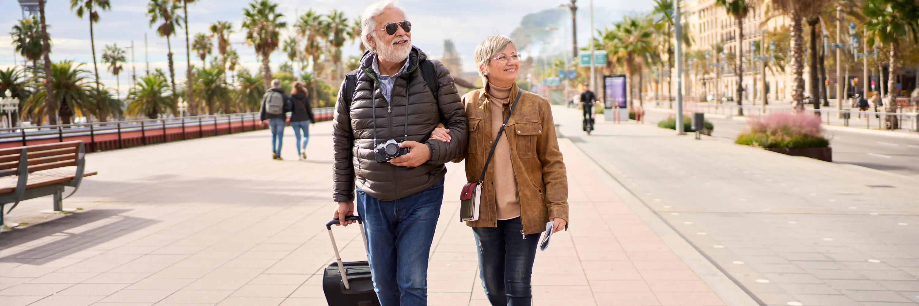 Smiling couple walking with luggage on vacation, reflecting the benefits of mobility prep for staying on your feet while traveling