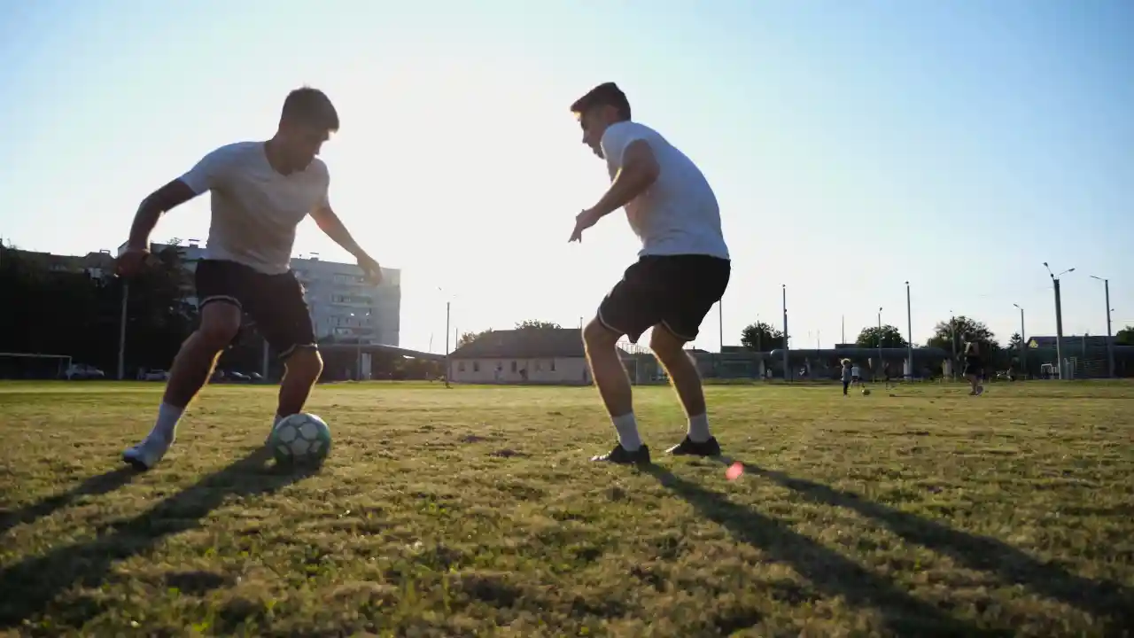 Two adults playing soccer at sunset, showcasing active weekend movement and the importance of mobility before pickup games