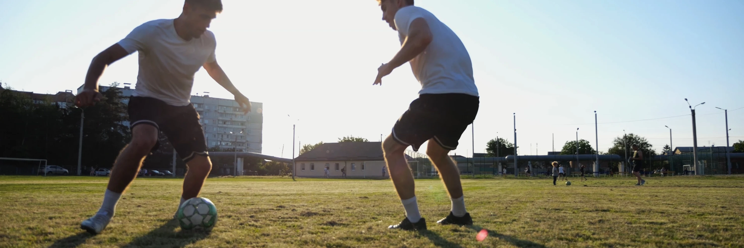 Two adults playing soccer at sunset, showcasing active weekend movement and the importance of mobility before pickup games