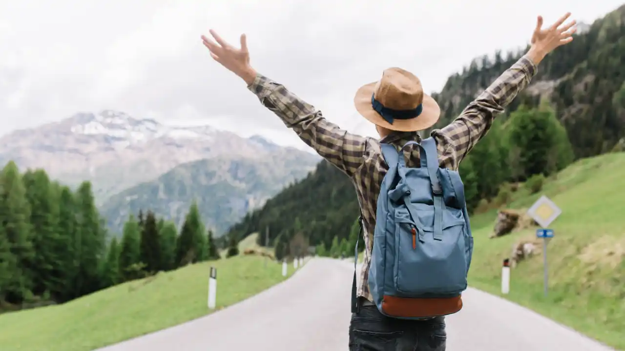 Traveler celebrating freedom on a scenic mountain road after staying energized with a daily movement routine while traveling.