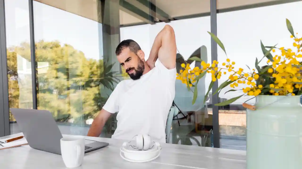 Man stretching his shoulder while working from home, taking a mobility break during a call.