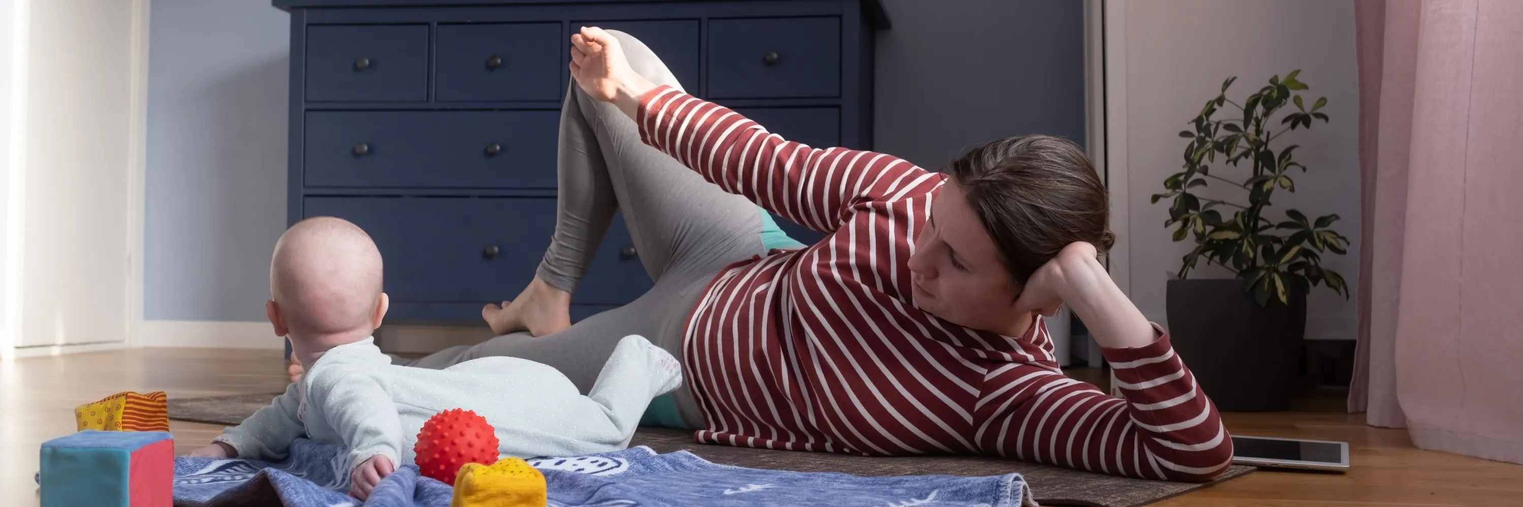 Parent doing a gentle floor stretch while playing with baby at home, incorporating mobility during family playtime.