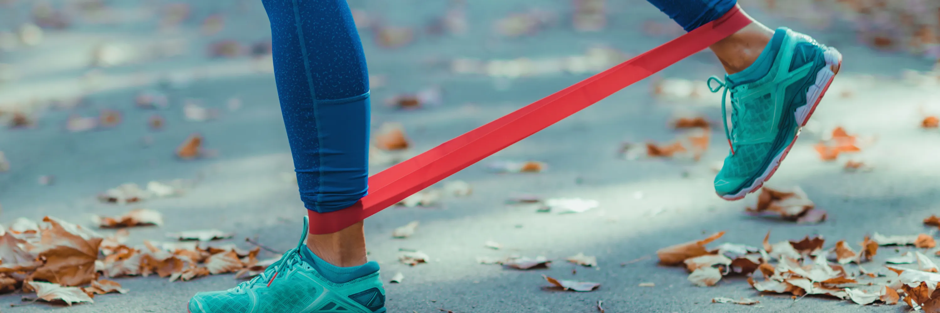 Close-up of traveler using a mini resistance band for leg mobility exercises outdoors in autumn.