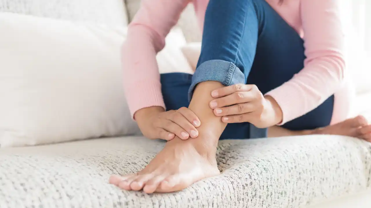 Close-up of a woman holding her ankle, highlighting foot and ankle health and mobility awareness.