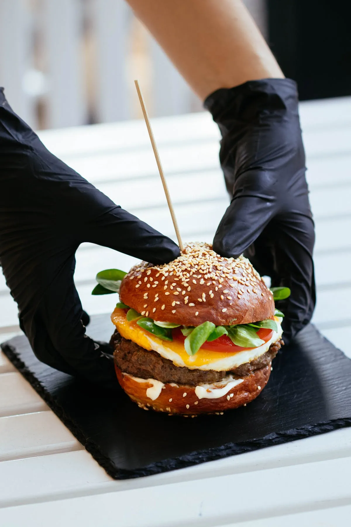 Two hands of the same person holding a burger