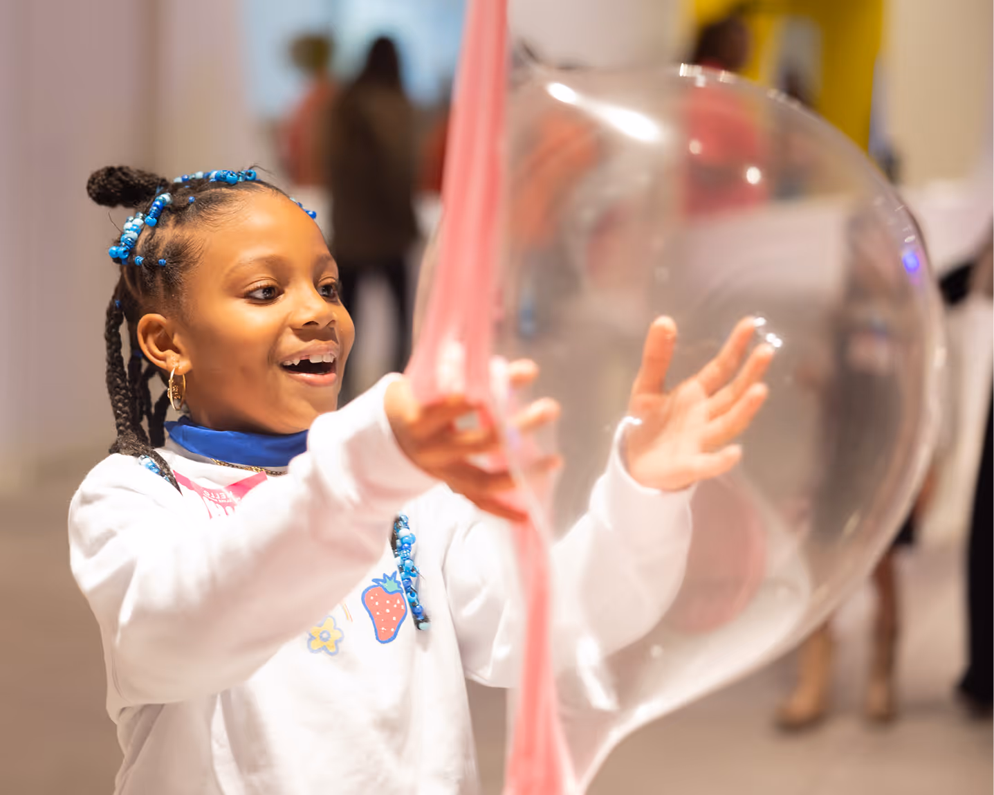 Smiling young girl with blue beads in her braided hair playing with a large clear bubble and pink slime.