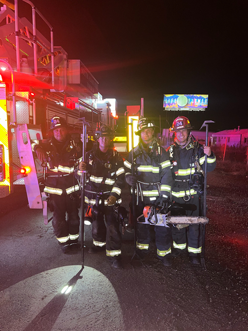 four firefighters standing in front of a firetruck