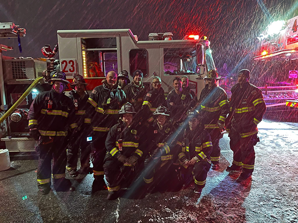 a group of firefighters standing in the rain in front of two fire trucks