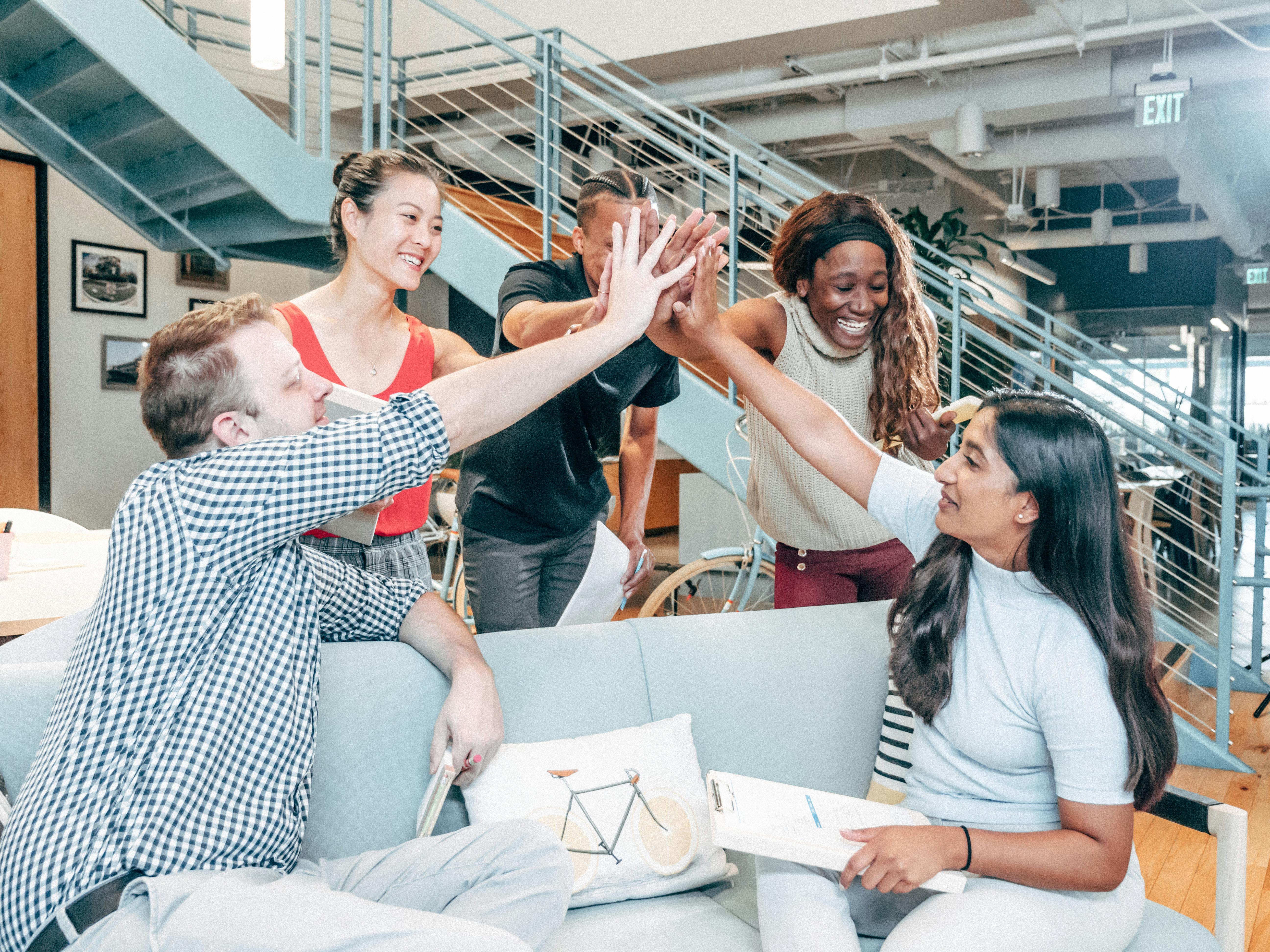 Diverse group of colleagues high-fiving in a modern collaborative office setting, smiling and celebrating together