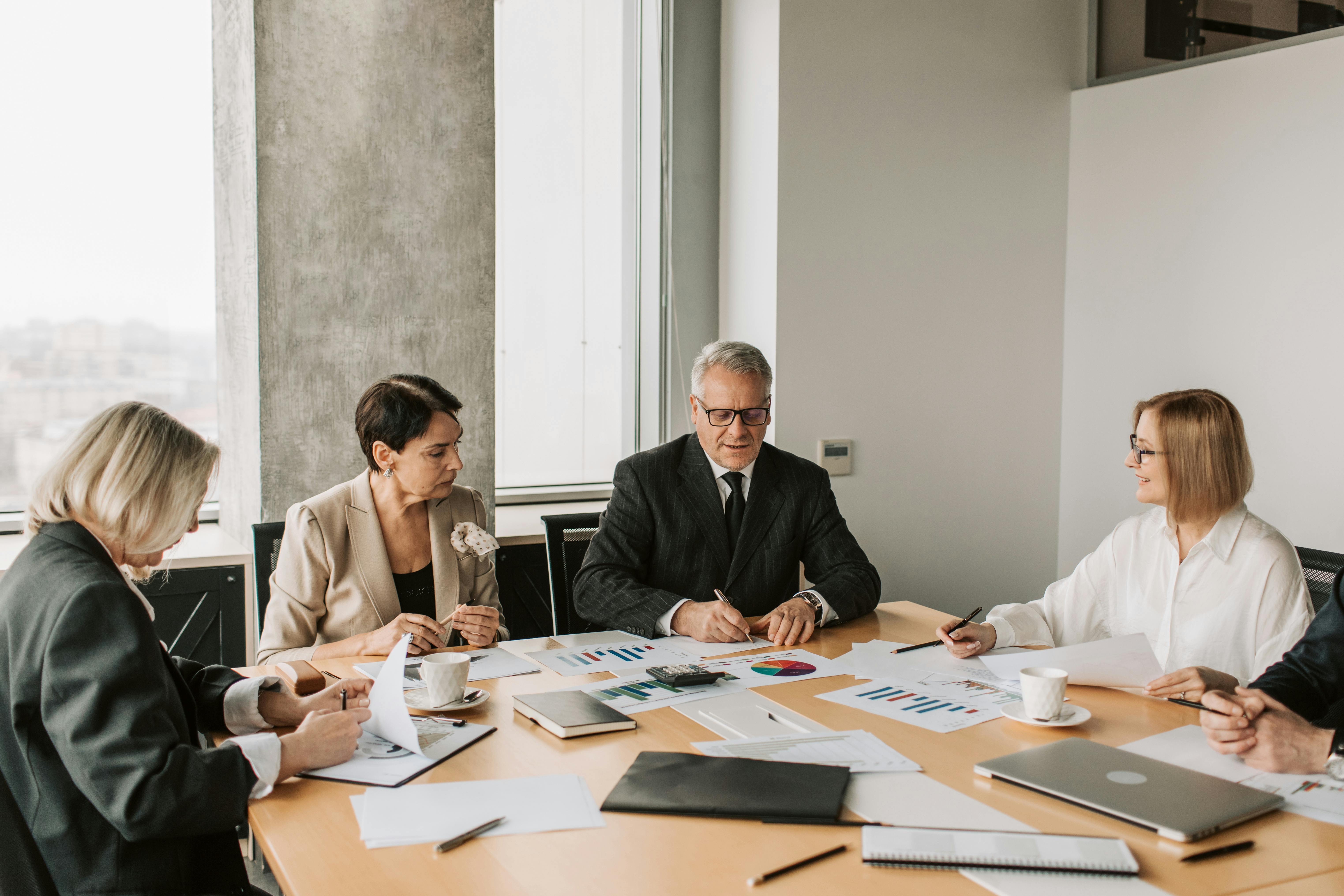 Corporate team seated around a conference table analyzing printed business reports and charts