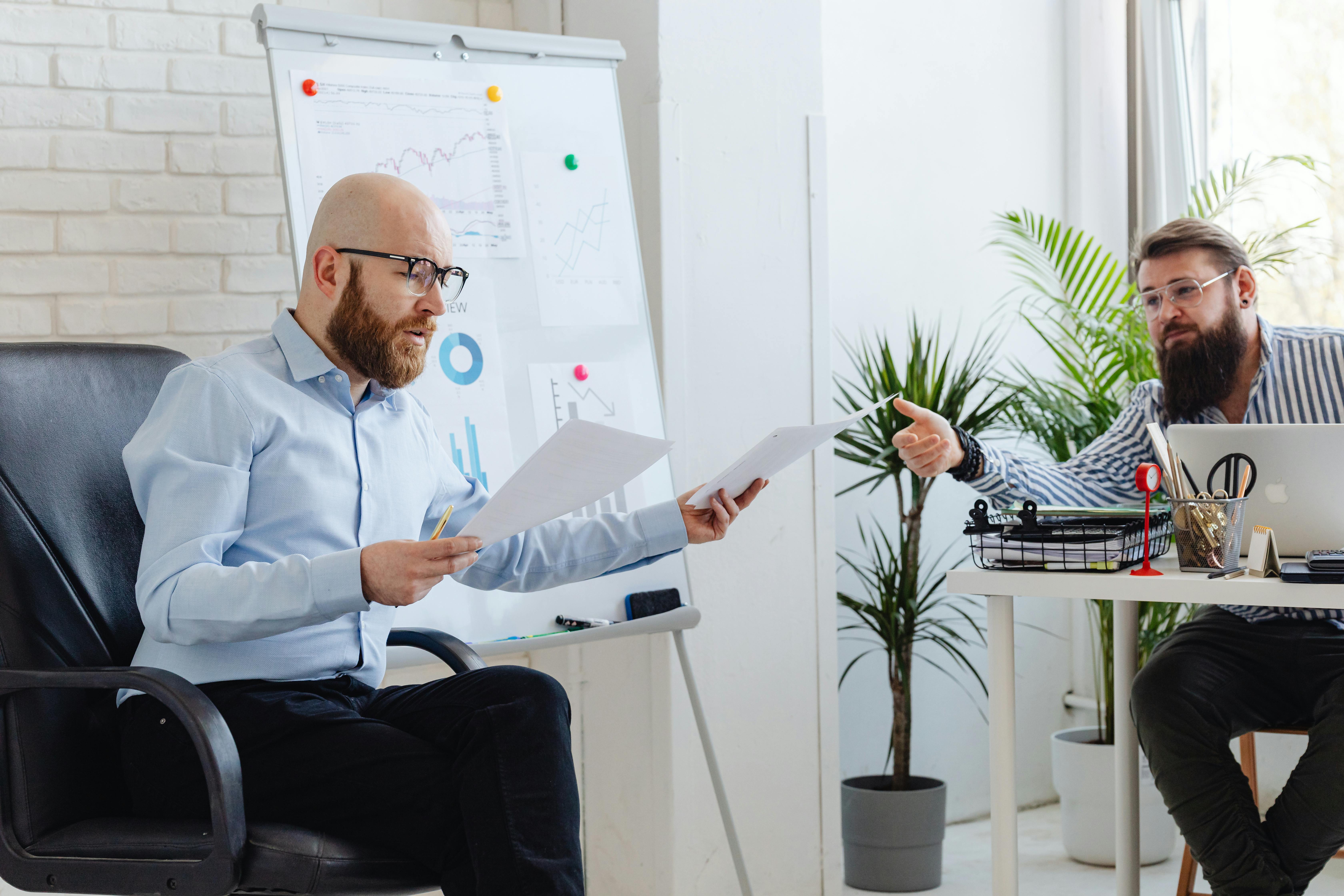 Two men in a modern office space having a business discussion in front of a whiteboard with graphs and data