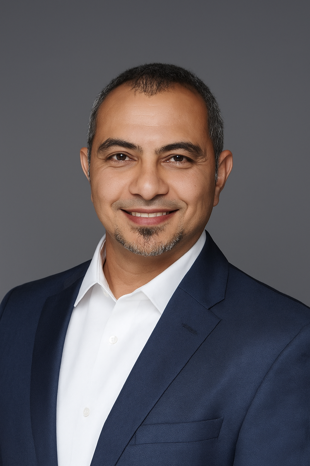Professional headshot of a smiling male consultant wearing a navy suit and white shirt against a grey background