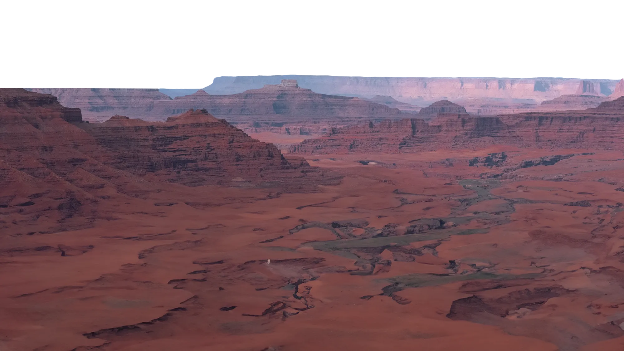 Expansive view of a red rock canyon landscape with winding riverbeds and layered cliffs under a hazy sky.