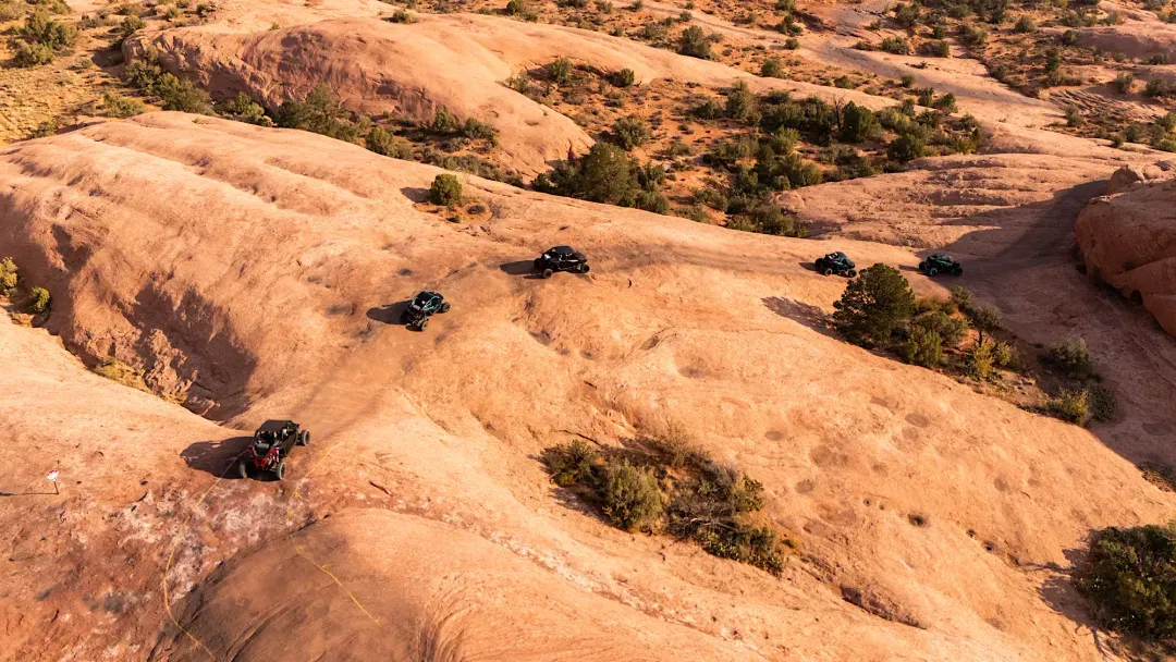 Five off-road vehicles driving across smooth, rocky desert terrain with sparse vegetation.
