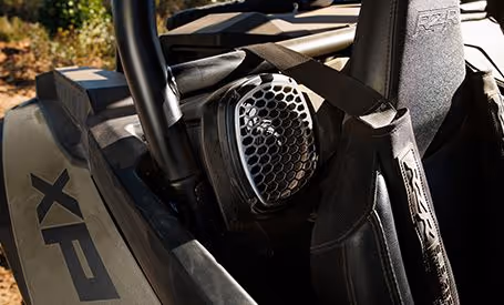 Close-up of a vehicle speaker mounted inside the roll cage near a black seat with a seatbelt.