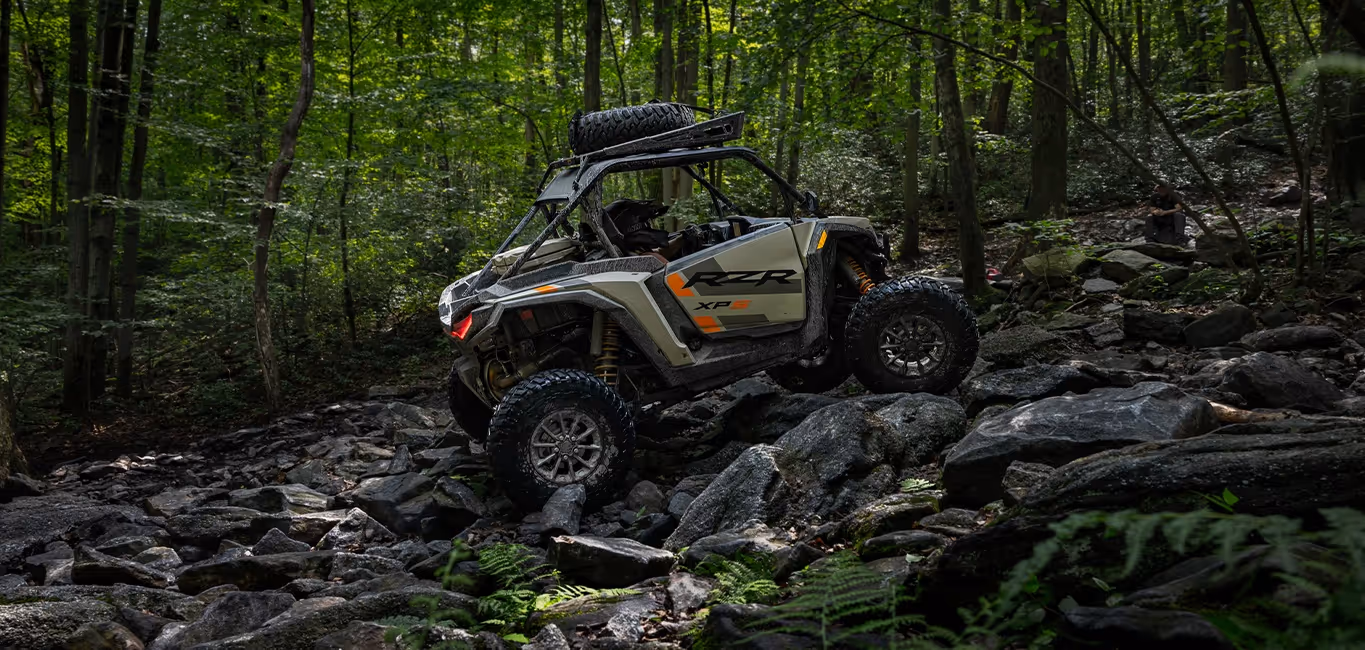 Off-road vehicle RZR XP navigating rocky terrain in a dense forest.