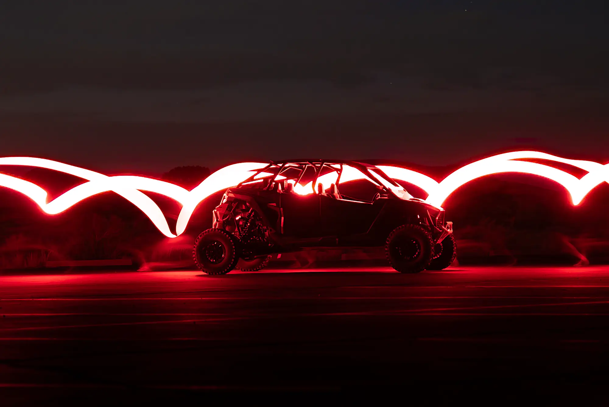 Off-road vehicle illuminated by red light trails at night.