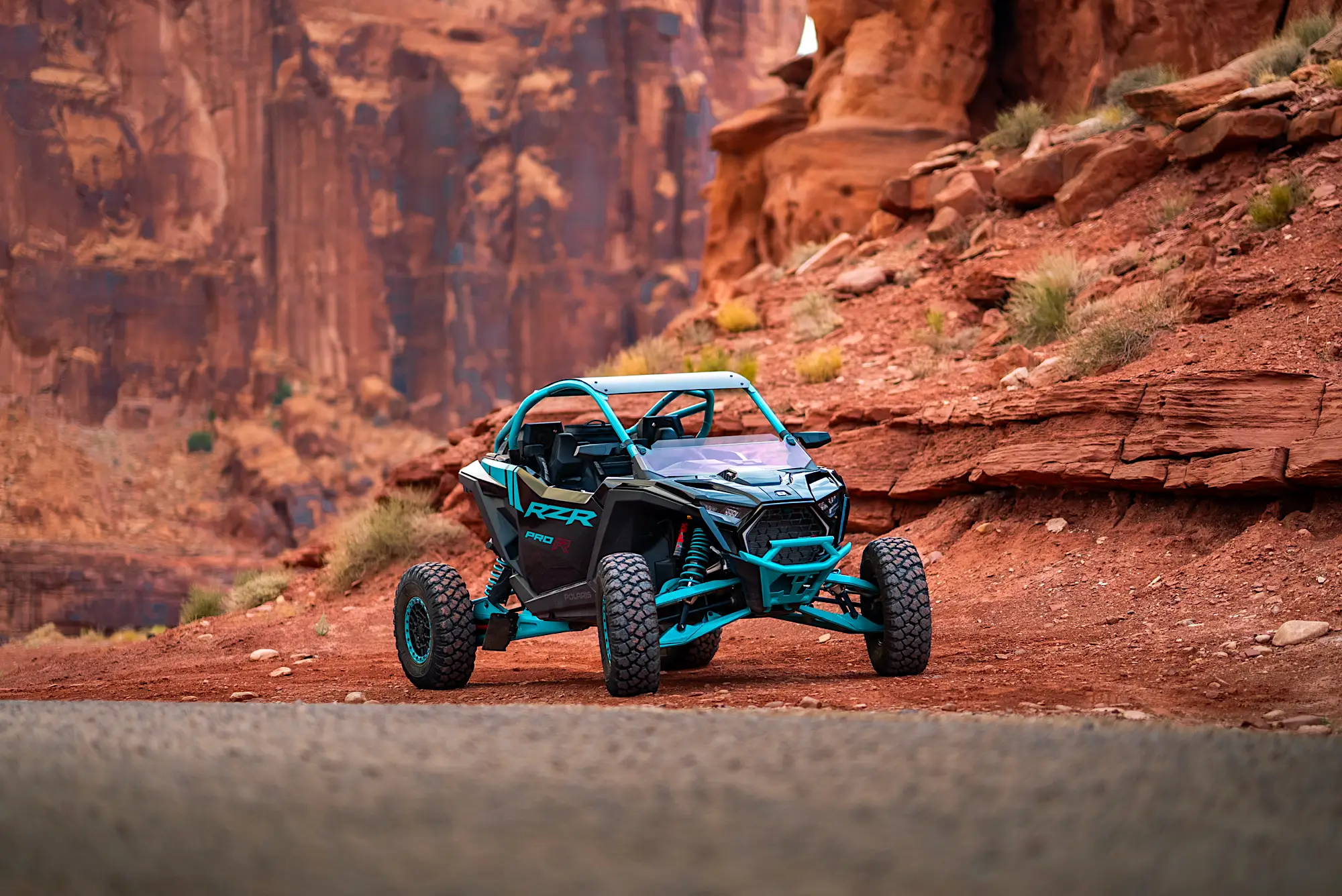 Blue and black Polaris RZR off-road vehicle parked on a desert trail with red rock formations in the background.