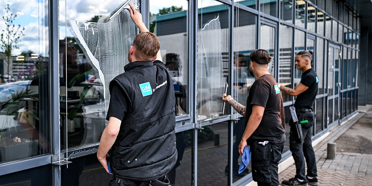 Drie DJM-medewerkers reinigen grote ramen van een bedrijfsgebouw met professionele glasbewassingstechnieken.