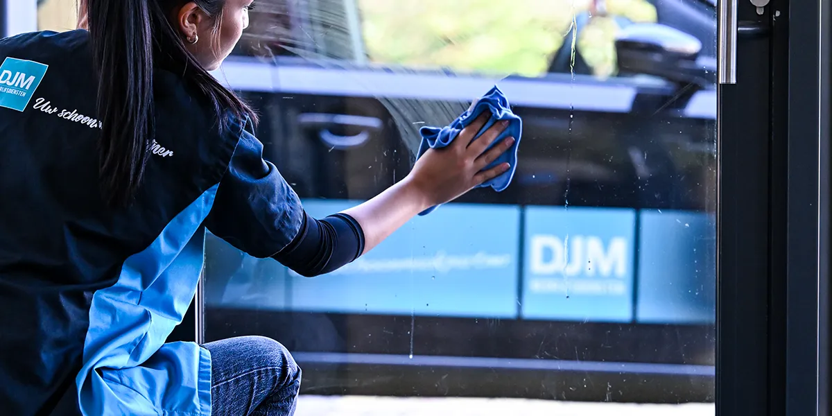 Drie DJM-medewerkers reinigen grote ramen van een bedrijfsgebouw met professionele glasbewassingstechnieken.