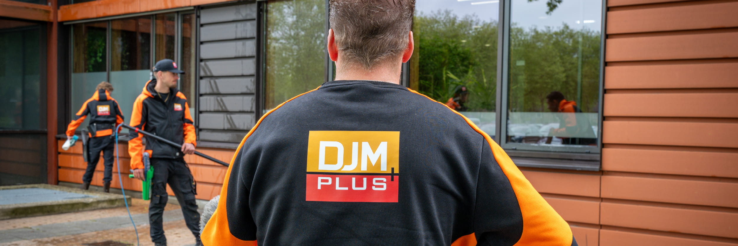 DJM-medewerker draagt een ladder bij een bedrijfsbus met DJM-logo, klaar voor werkzaamheden op locatie in de vastgoedsector.