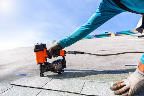 Contractor using a nail gun to install new asphalt shingles as part of a professional roof replacement.