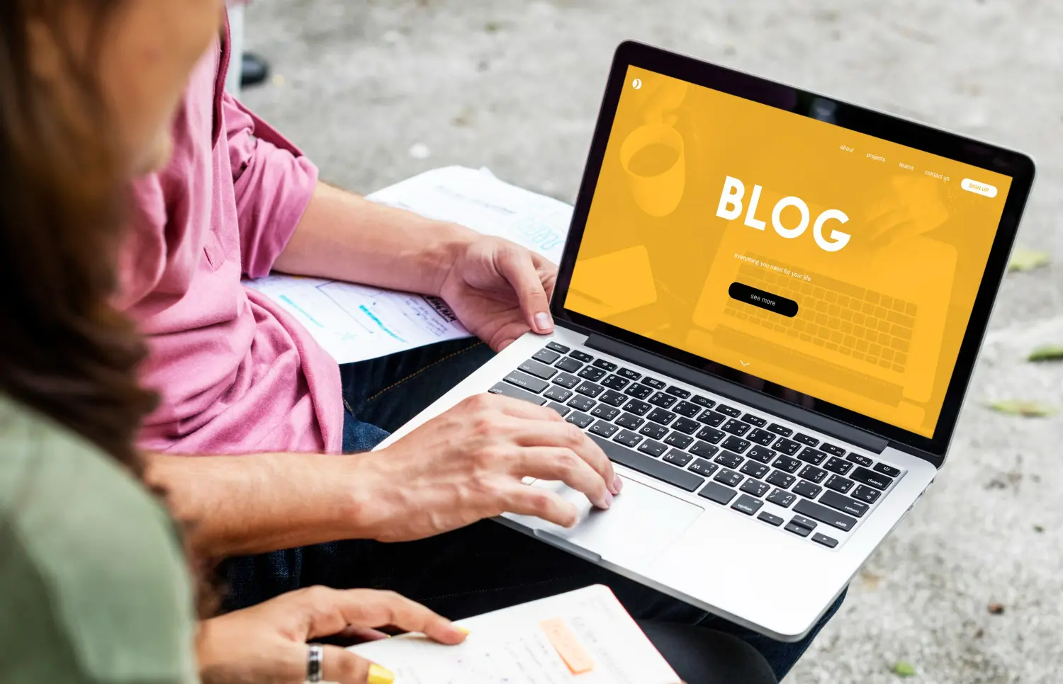 Two people collaborating outdoors on a laptop screen displaying the word “Blog,” symbolizing teamwork in content marketing and evergreen content planning