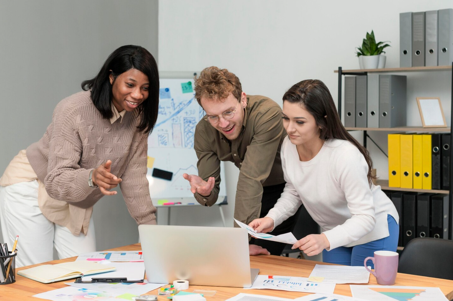 Three individuals gathered around a laptop, engaged in discussion and collaboration for rehab center marketing