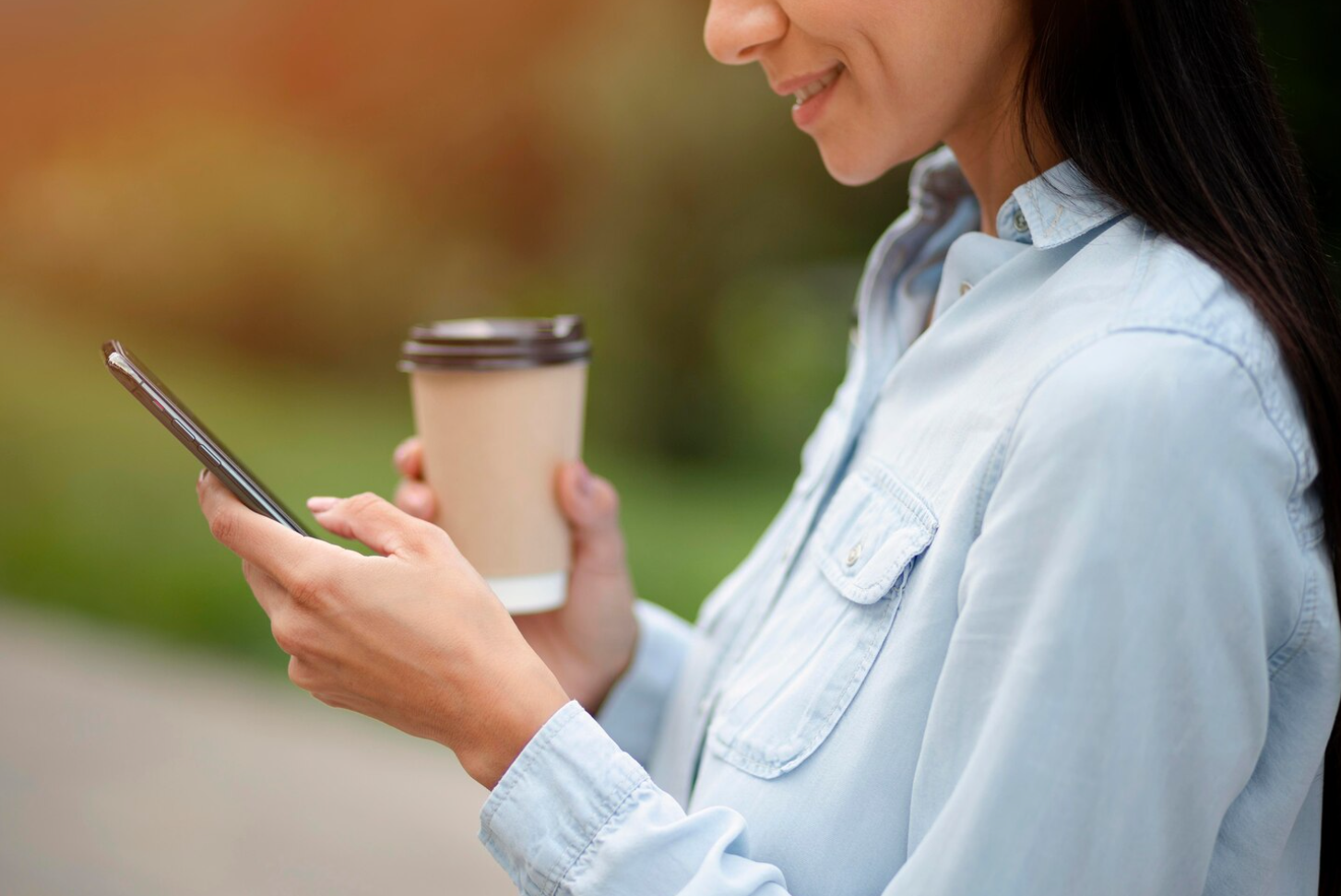 A woman holding a cup while looking at her phone, focused and engaged as she explores an addiction treatment website.
