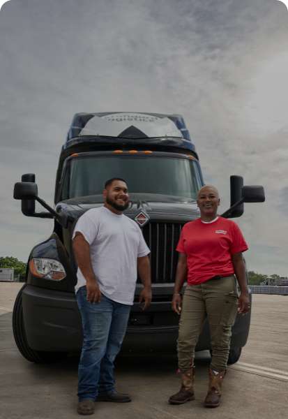 Two workers smiling in front of a Standard Logistics truck outside.