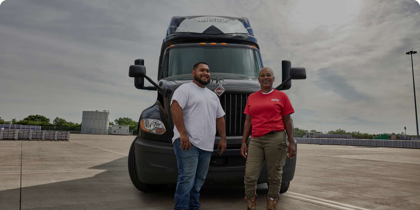 Two workers smiling in front of a Standard Logistics truck outside.