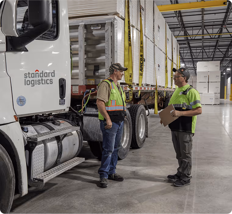 Workers standing beside a Standard Logistics truck inside a warehouse.