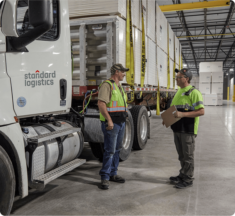 Workers standing beside a Standard Logistics truck inside a warehouse.