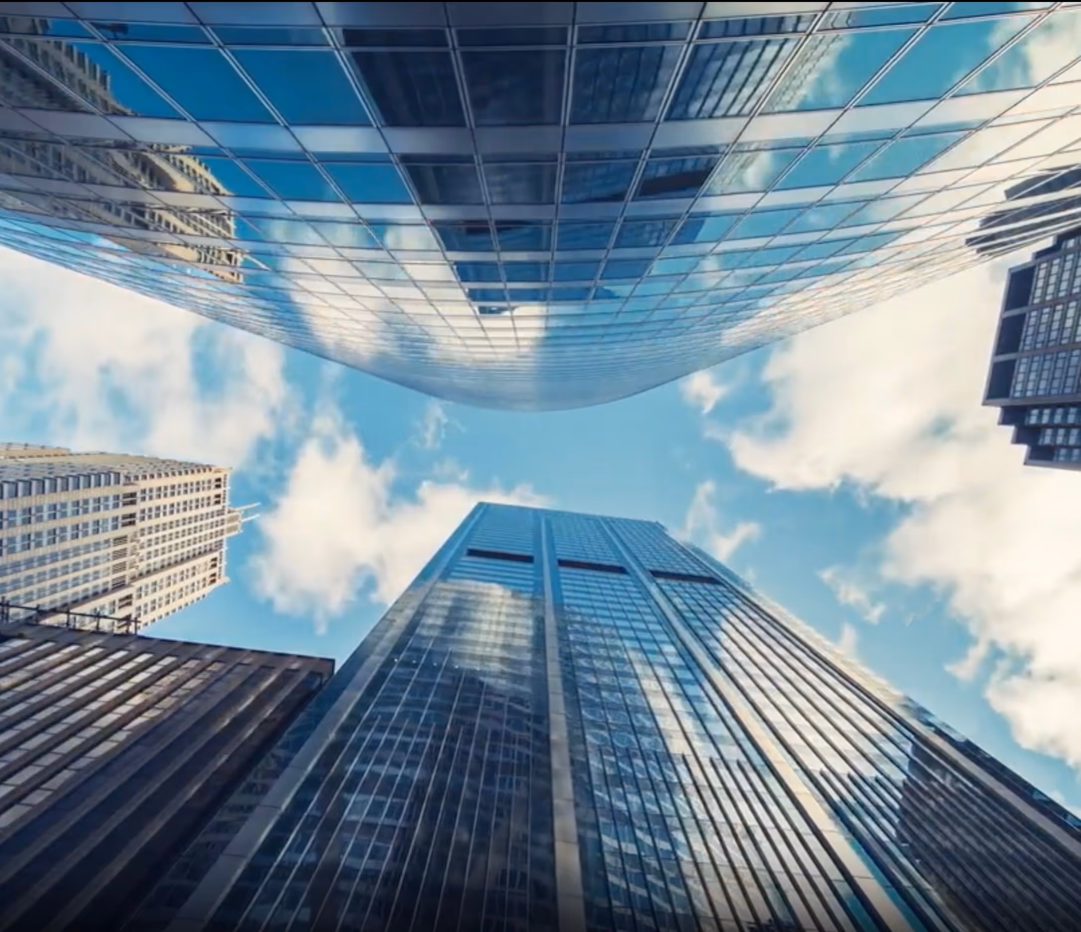 Looking up at tall skyscrapers with glass windows reflecting a blue sky with clouds.