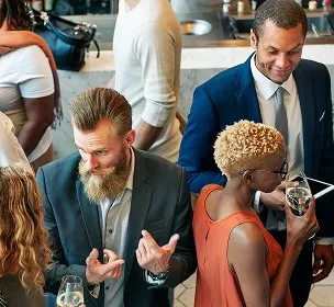 In a lively gathering, diverse professionals in formal attire converse and hold drinks, creating a warm, engaging social atmosphere.