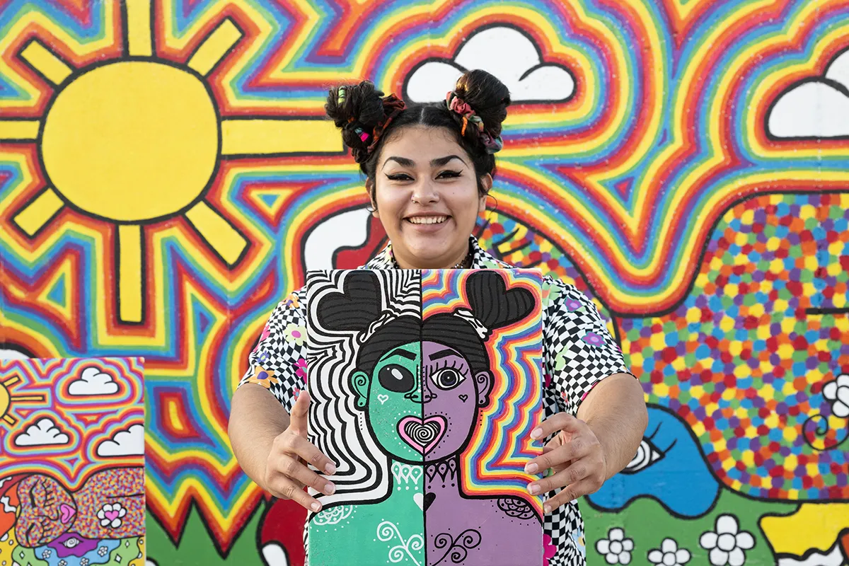 A female artist holds up a painting that inspired her Grand Island mural.