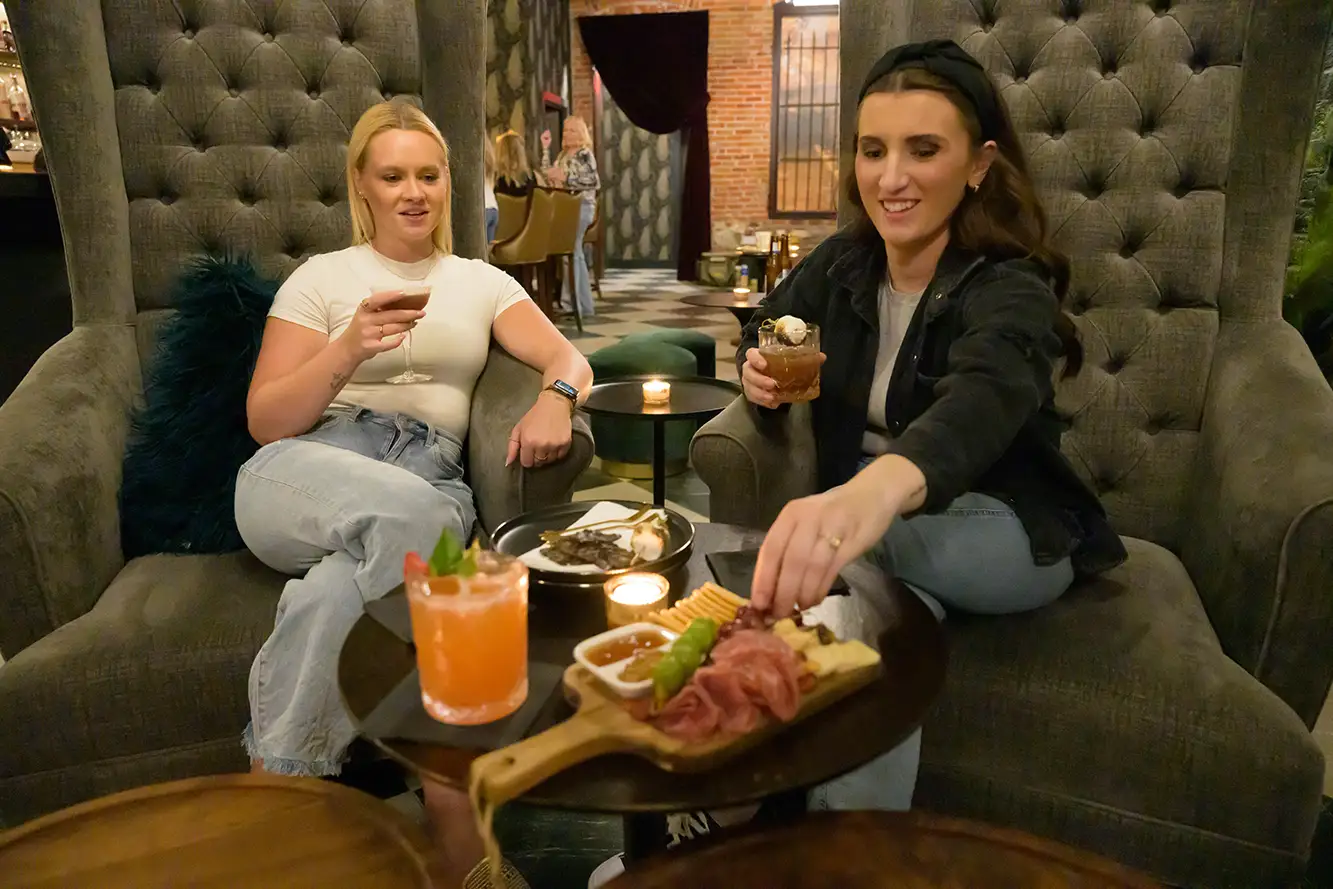 Two women sip cocktails while eating charcuterie in a Grand Island bar.