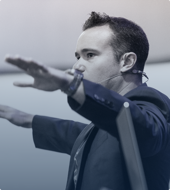 Man wearing a headset microphone with arms extended forward, appearing to speak or present.