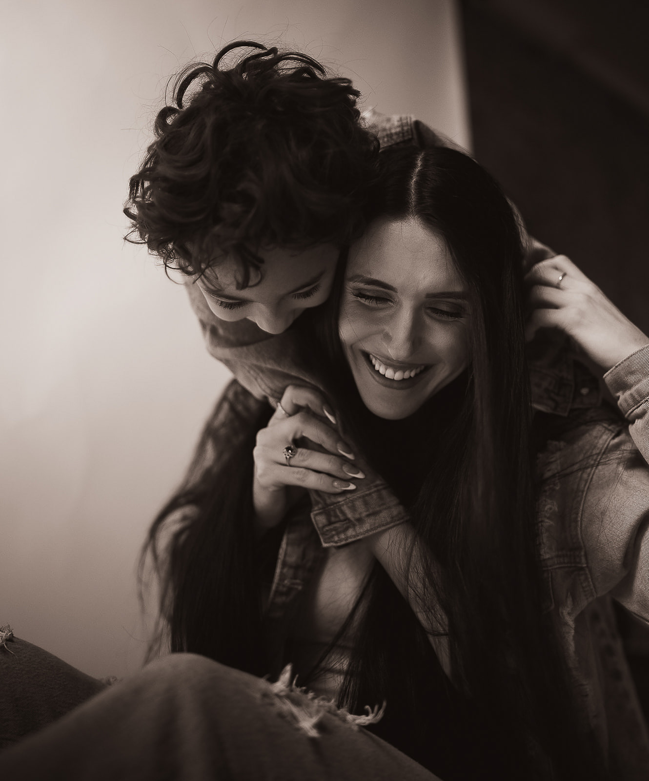 Smiling woman with long hair receiving a hug from a child with curly hair, both wearing denim jackets.