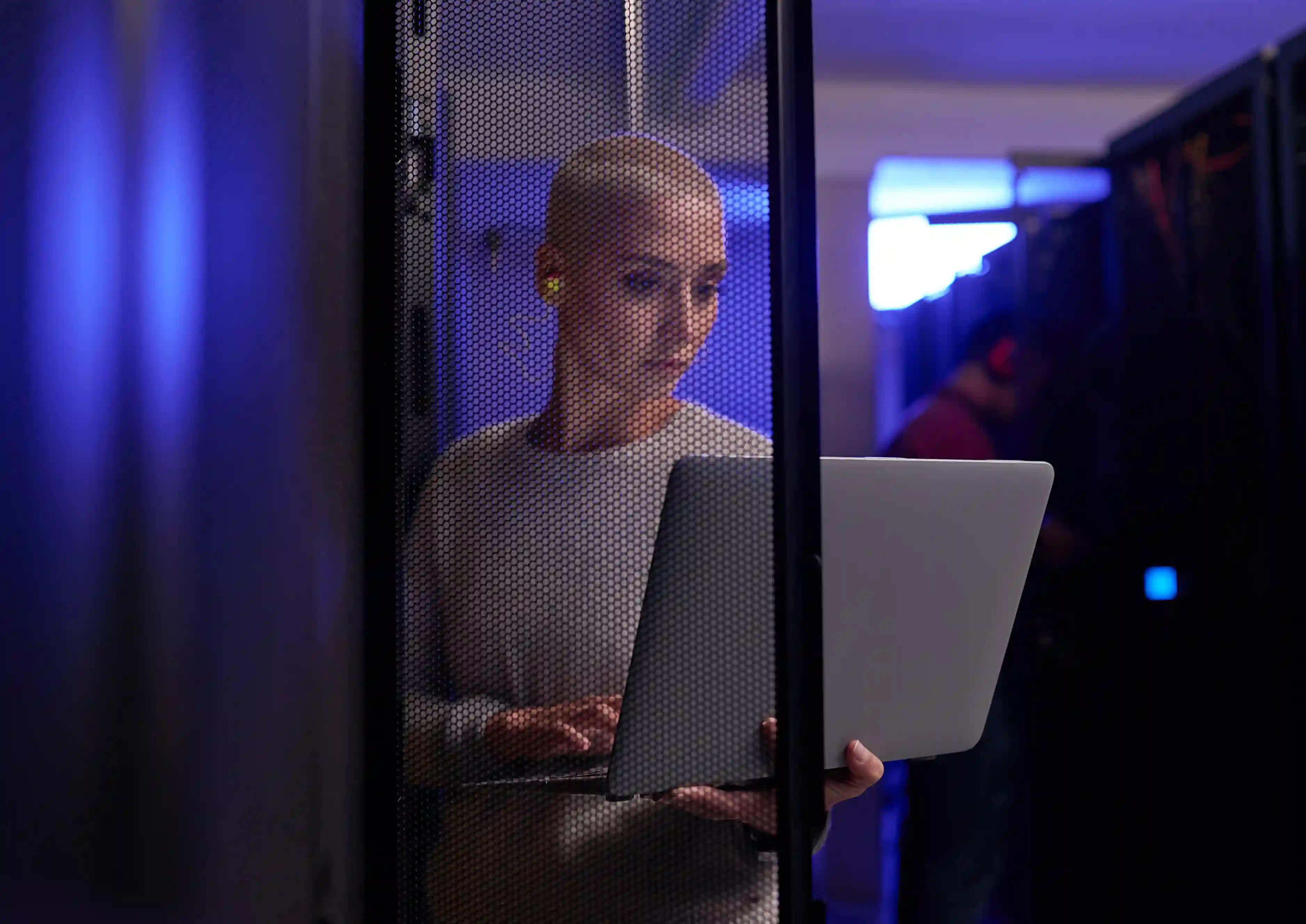 A woman in a server room looking at a laptop.