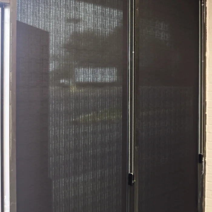 Black solar screen shades partially drawn on glass doors
