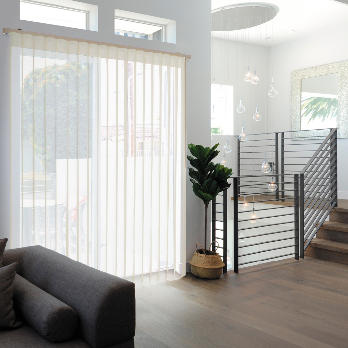 Corner of a living room with tall vertical shades over large windows allowing filtered daylight in