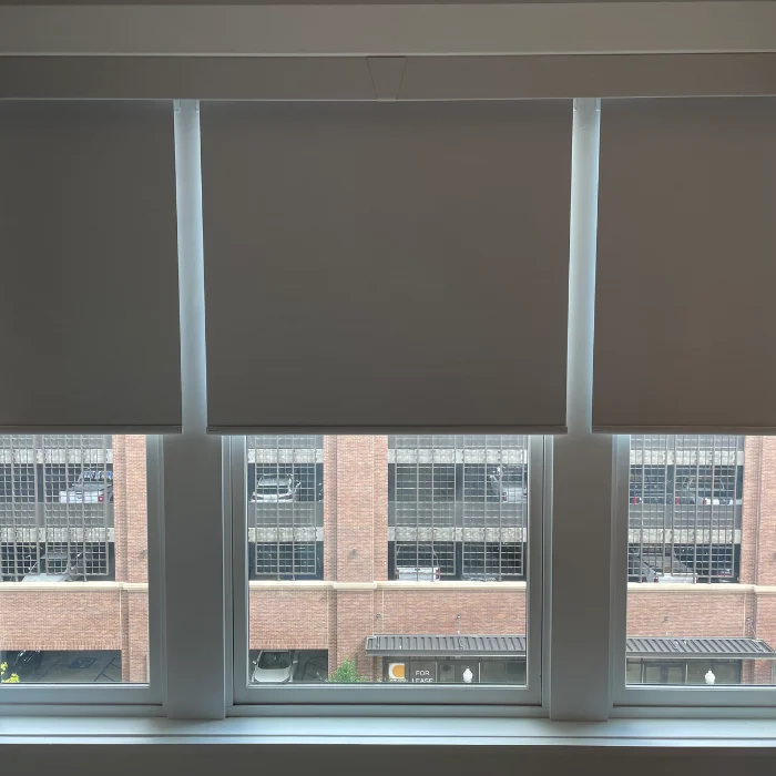 Triple window with closed roller shades overlooking brick building